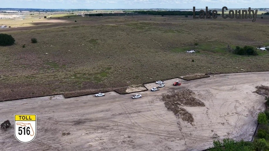 SR 516 Work in Lake County Aerial view of a dirt lot with several white pickups parked along a road, open field beyond, and a Lake County watermark in the top right; Toll 516 shield at bottom left.
